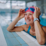 A happy senior woman in swimming pool, leaning on edge.